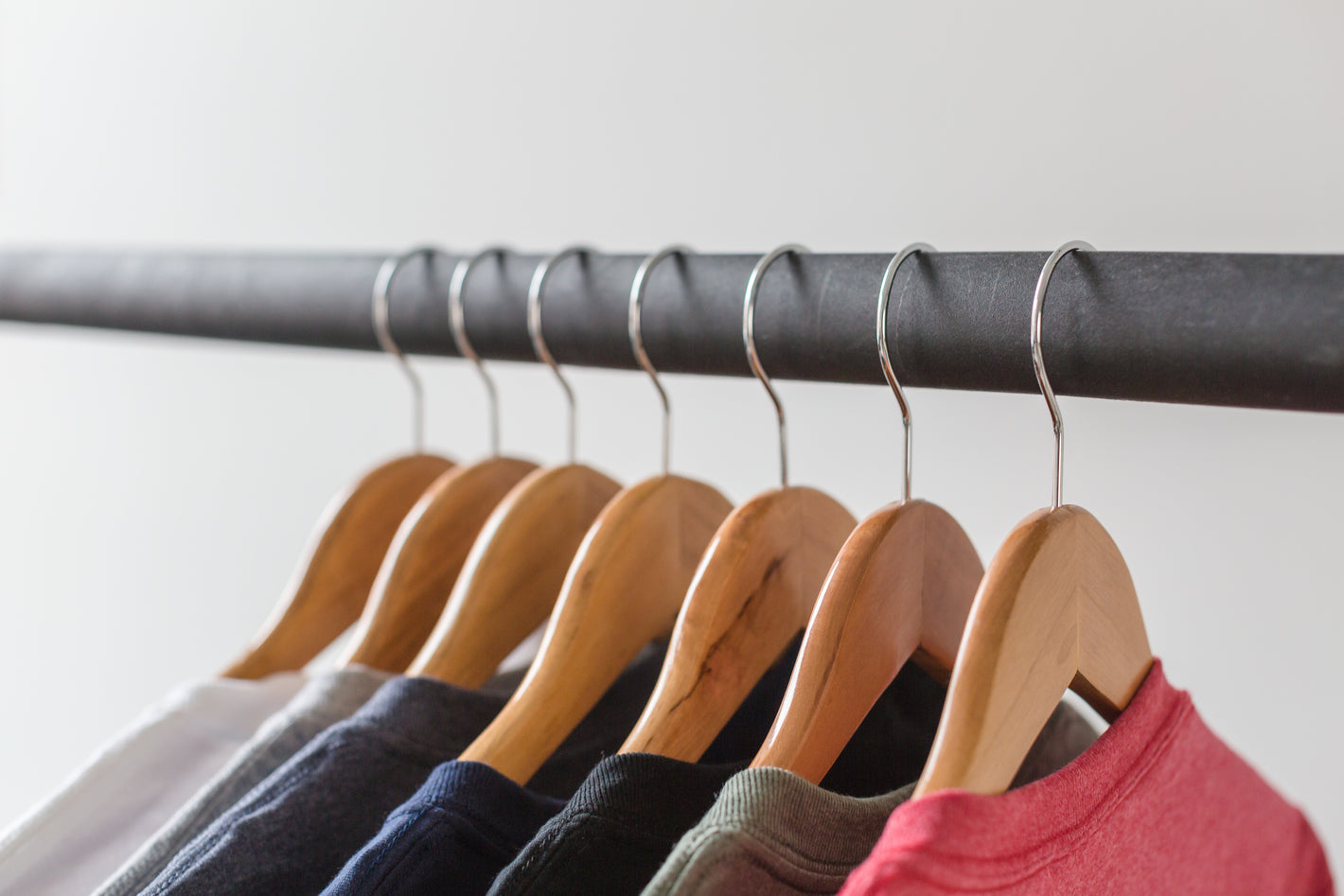 7 colored t-shirts hanging on wooden hangers